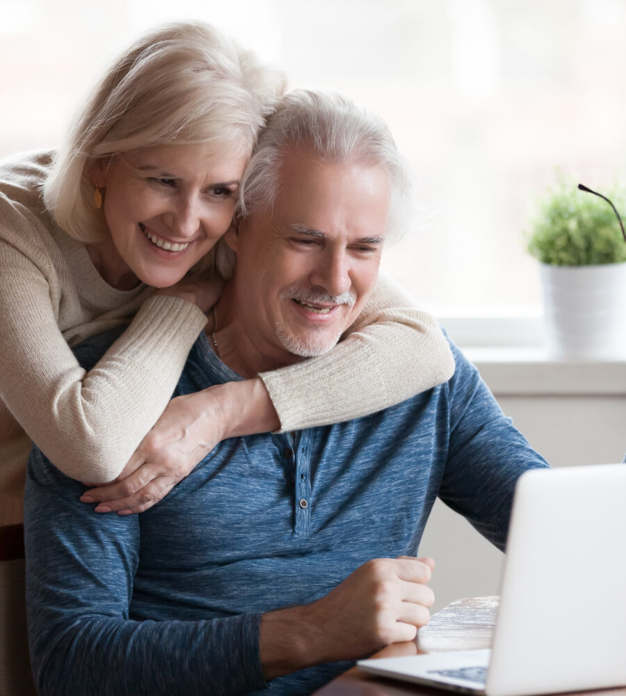 Eine Frau umarmt einen Mann der an Laptop etwas betrachtet