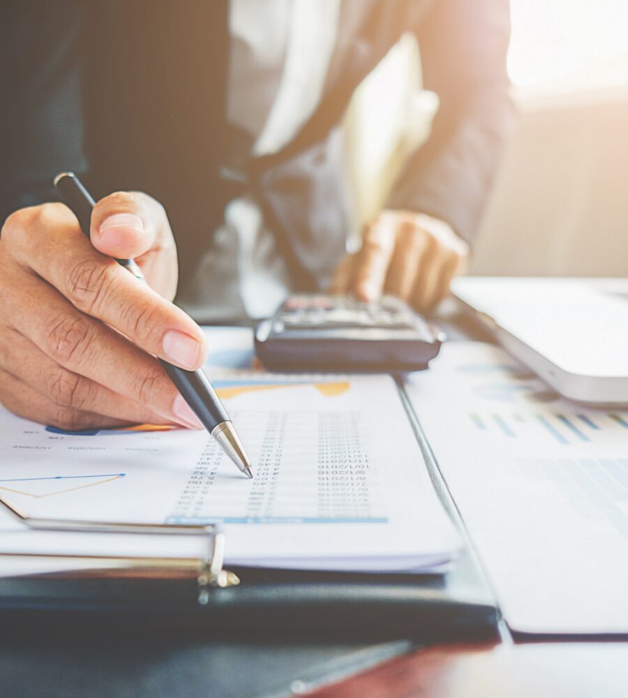 Mann im Anzug rechnet mit einem Taschenrechner eine Tabelle nach auf dem Schreibtisch